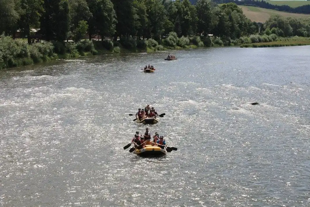 Grupa osób w kolorowych pontonach spływa rzeką otoczoną drzewami, uprawiając rekreację na świeżym powietrzu.