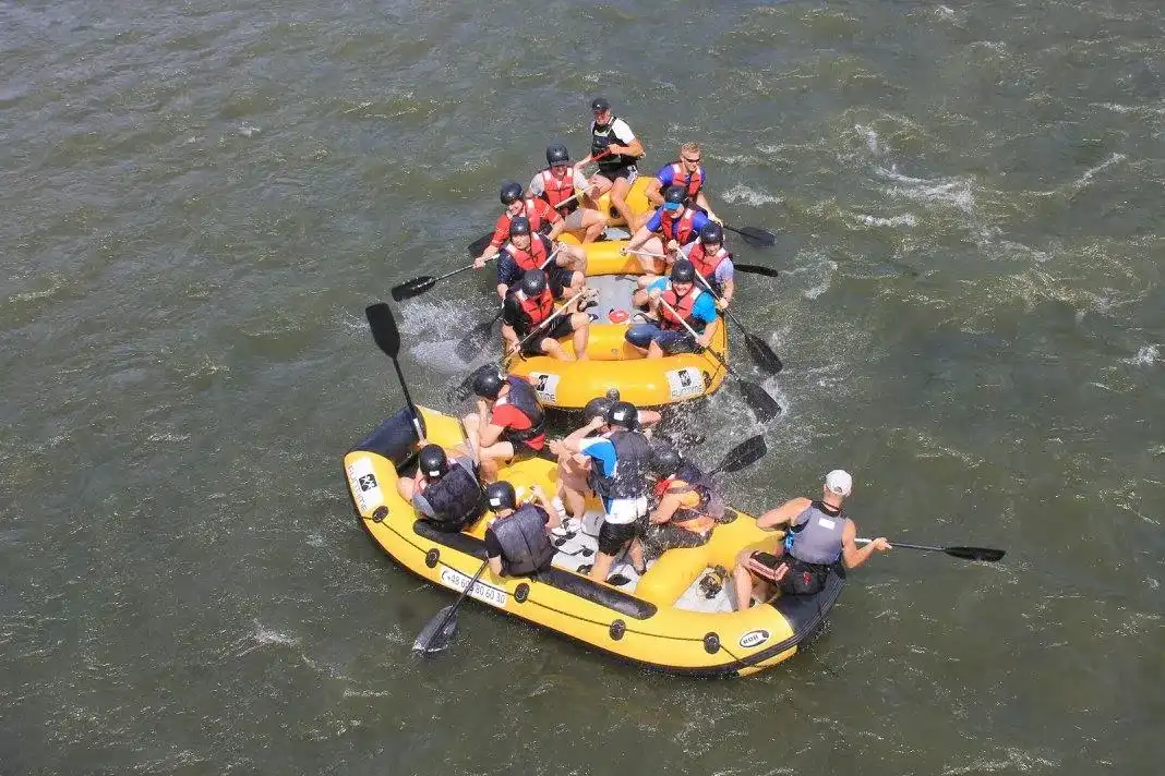 Grupa osób znajduje się w pontonie na jeziorze, w kamizelkach ratunkowych i wiosłuje, ciesząc się rekreacją na świeżym powietrzu.