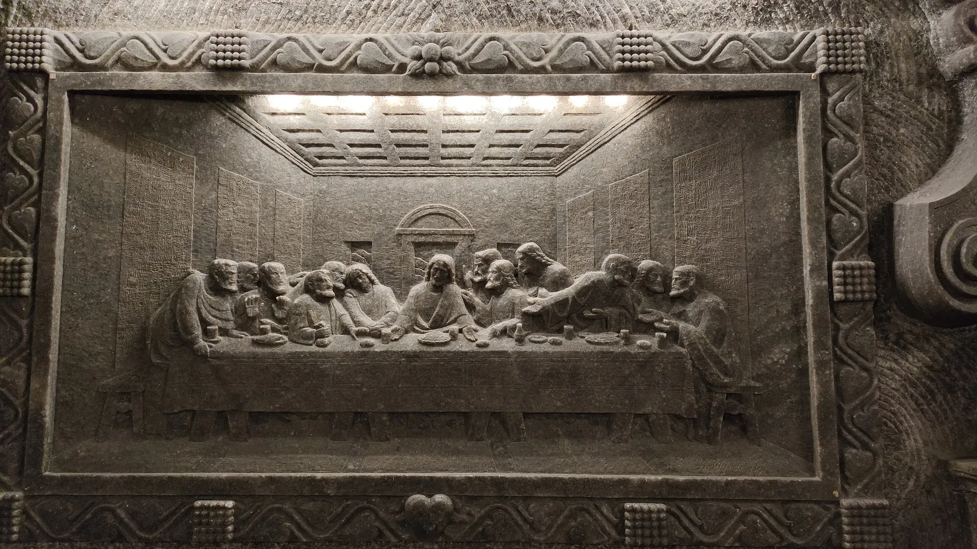 Kamienna rzeźba przedstawiająca wiele postaci zebranych wokół stołu, reprezentująca Ostatnią Wieczerzę. Szczegóły ukazują misterną rzeźbę i pracę reliefową, podkreślając artyzm dzieła. Obraz jest czarno-biały, co podkreśla jego historyczne znaczenie jako eksponatu w muzeum.