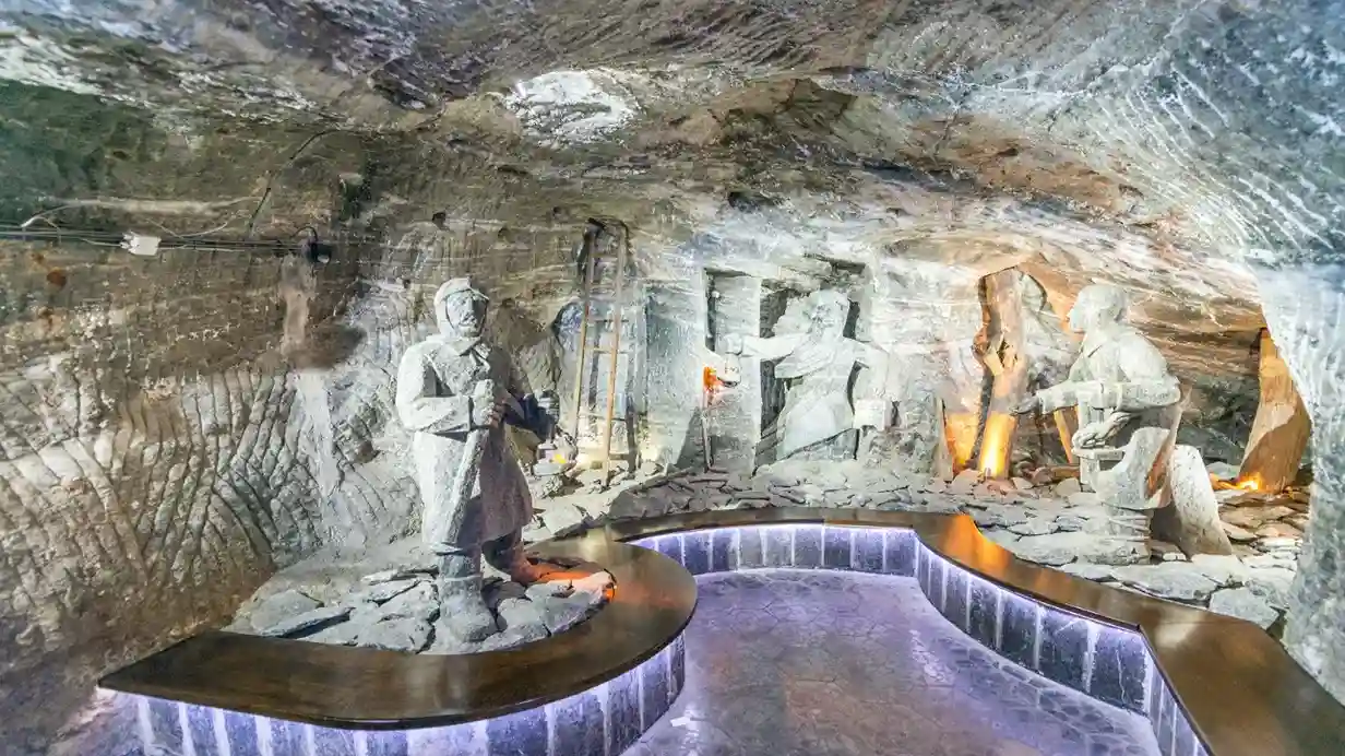 Statua znajduje się w jaskini, otoczona skalnymi ścianami i naturalnymi elementami. Słabe oświetlenie podkreśla kontury statuy na tle surowej scenerii.