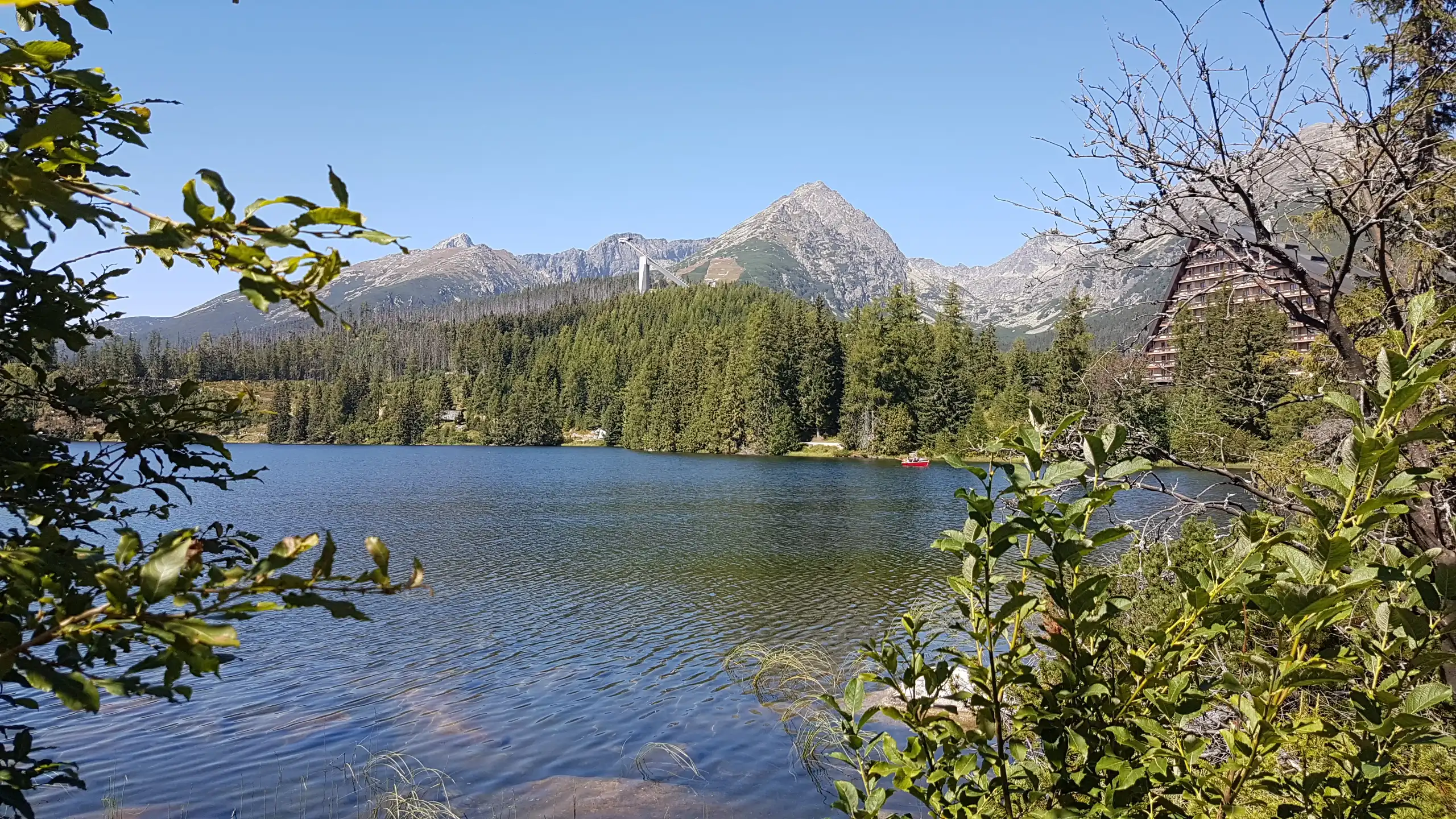 Dwie łodzie na jeziorze otoczonym górami, z krystalicznie czystą niebieską wodą i jasnym niebem. Scena oddaje esencję rekreacji na świeżym powietrzu i spokoju.