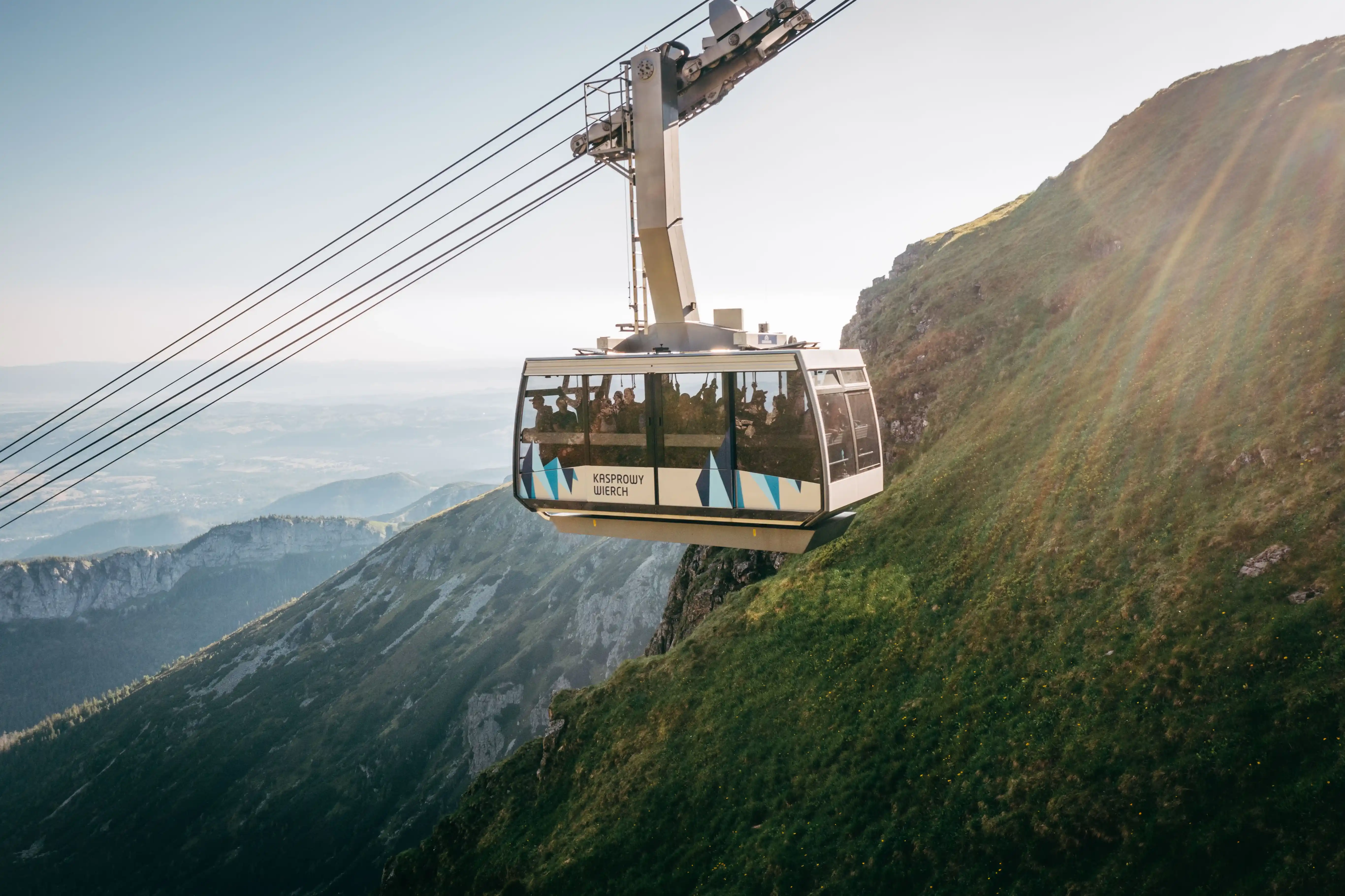 Kolejka linowa wspinająca się na górę, otoczona czystym błękitnym niebem i surowym terenem.