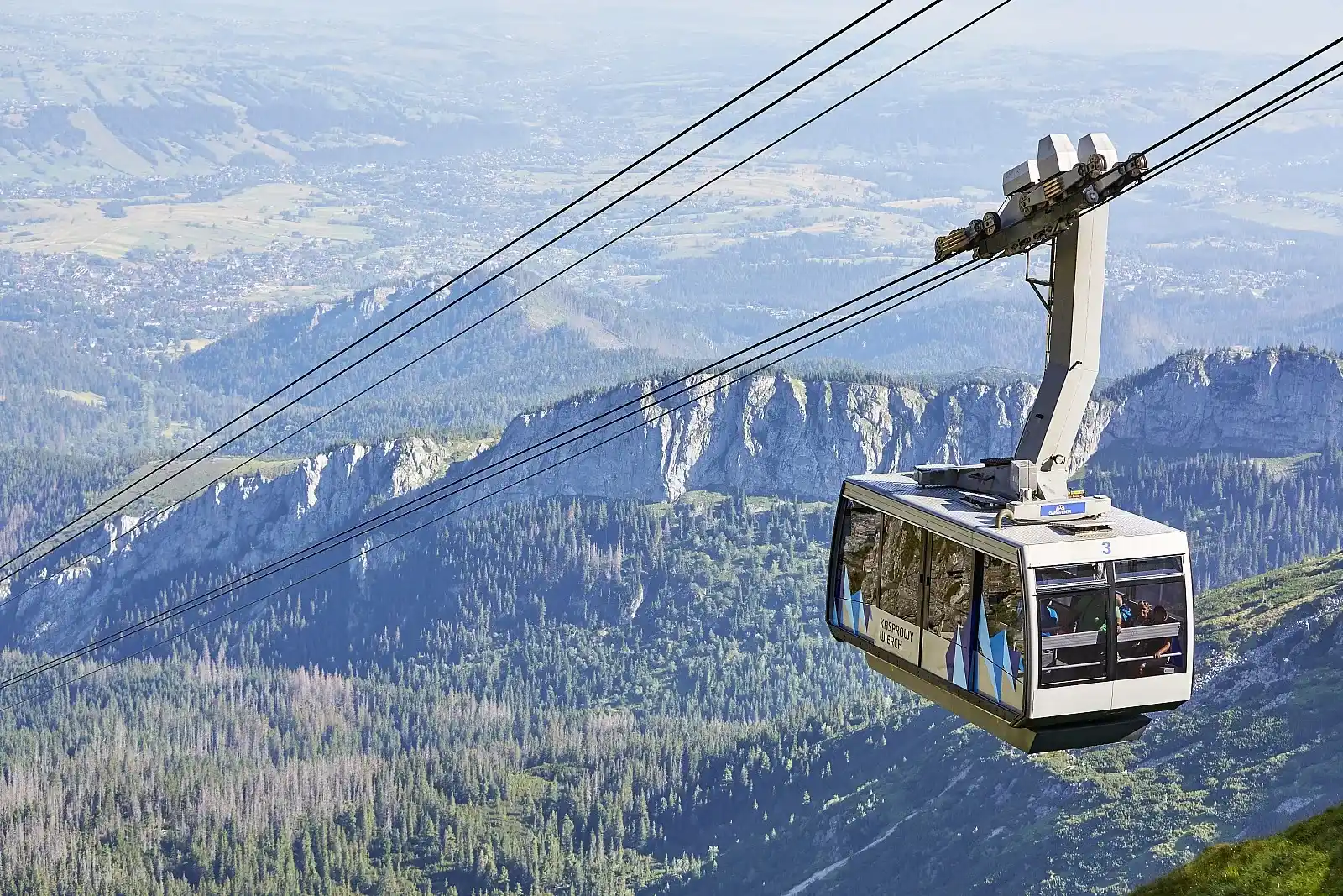Kolejka linowa zawieszona nad doliną, otoczona górami, zapewniająca transport w plenerze.