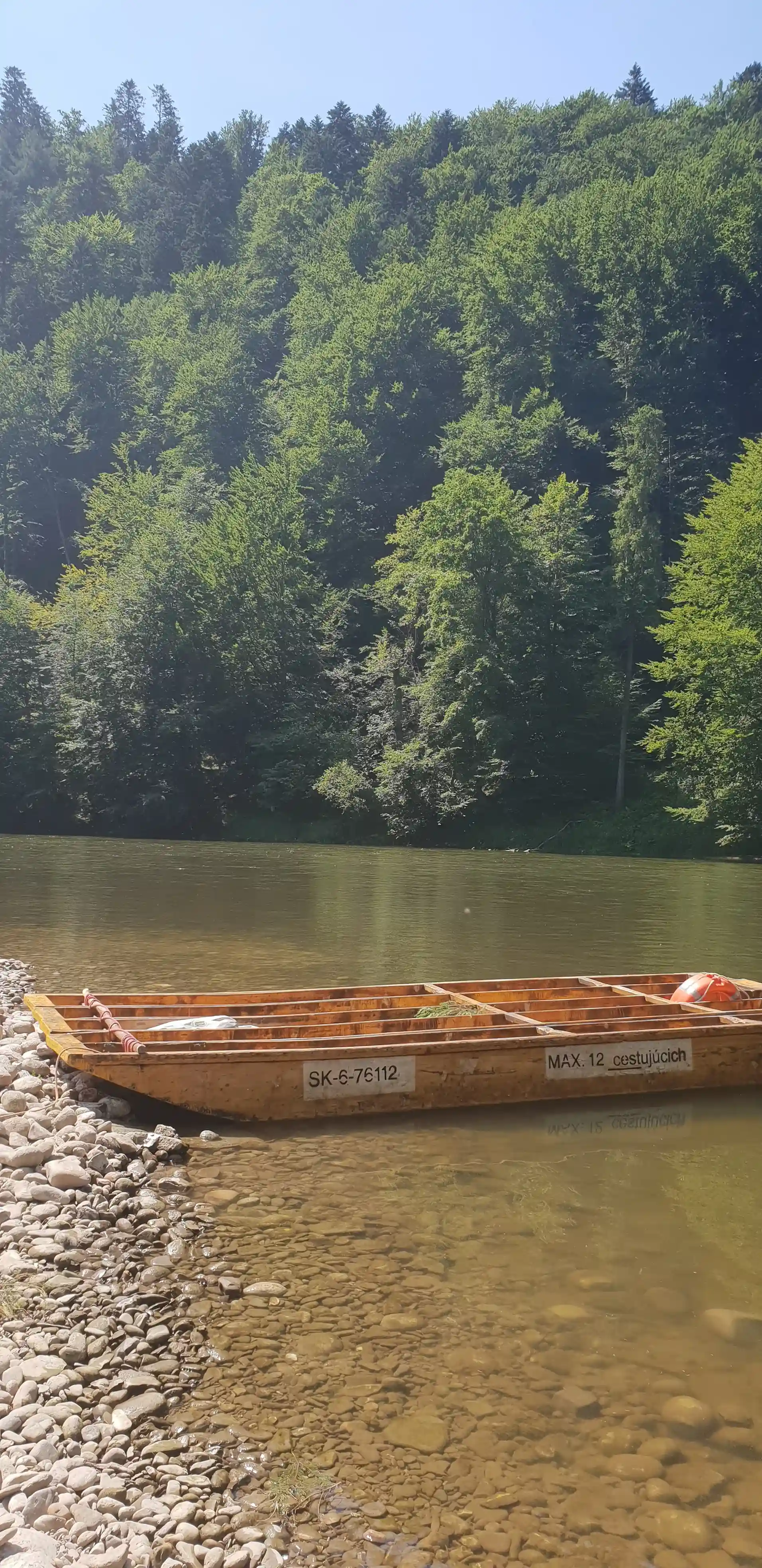 Łódź unosząca się na rzece otoczonej drzewami i górami, reprezentująca aktywność na świeżym powietrzu i transport wodny.